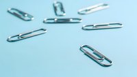 Silver metal paper clips scattered on light blue background for office supplies and business organization concepts.