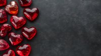 Red glass hearts scattered on dark textured background with copy space. Romantic concept for Valentine's Day, love messages, and greeting cards.