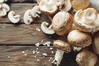 Fresh brown champignon mushrooms and sliced pieces on rustic wooden background with soft natural lighting, macro food photography for cooking blogs.