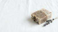 Natural handmade lavender soap bar with dried herbs on white marble surface for spa and skincare routine.