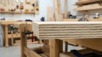Plywood edge detail in carpentry workshop with woodworking tools and workbenches in blurred background for construction and furniture making projects.