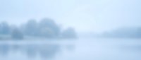 Soft blurred lake landscape with misty morning fog and calm water reflection creating peaceful atmospheric background for meditation and wellness content.
