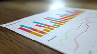 Colorful business graph showing financial data analysis with bar charts and line graphs on white paper document against wooden desk surface.