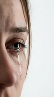 Close-up of young Caucasian woman with green eyes crying, tears streaming down face showing raw human emotion and vulnerability on neutral background.