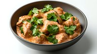 Creamy butter chicken curry with tender meat pieces in rich tomato-based sauce garnished with fresh cilantro leaves served in dark ceramic bowl on light background.