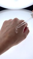 Hand holding glass dropper with clear serum drop for skincare routine and beauty treatment on clean white background.