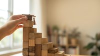 Hand placing wooden block with graduation cap on top of stacked blocks representing education achievement and academic success in bright indoor setting.