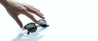 Elegant female hand reaching for stylish tortoiseshell sunglasses on white background, showcasing trendy eyewear for fashion and retail use.