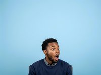 Man with dark skin tone and short black hair wearing navy sweater expressing surprise or shock against blue background for advertising and commercial use.