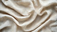 Soft beige linen fabric with gentle folds and natural texture creates elegant wavy pattern. Natural eco-friendly material background for fashion and interior design.