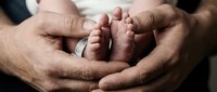 Adult male hands cradling newborn baby feet in tender moment, symbolizing parenthood, family bonding, and new life for healthcare and family-themed designs.