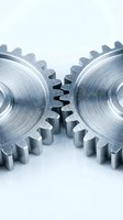 Two interlocking metal gears with brushed steel finish meshing together on white background representing teamwork and mechanical precision in industry.