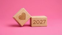 Wooden blocks with heart symbol and 2027 year number on pink background, representing love and new year planning.