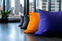 Vibrant orange and purple decorative throw pillows on dark wooden floor against modern city window background, creating cozy home atmosphere.