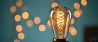Vintage Edison bulb glowing with warm filament against teal background with golden bokeh lights for cozy interior design and lighting concepts.