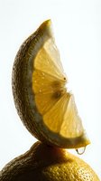 Juicy lemon slice balanced on whole lemon with dripping drop, glowing yellow citrus flesh and textured peel on light background.