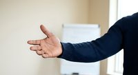 Professional businessman extending open hand for handshake in modern office environment, representing partnership and business cooperation opportunities.