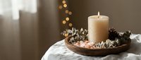 Cozy winter candle arrangement with pinecones and cotton branches on wooden tray creating warm holiday atmosphere for home decoration and seasonal styling.