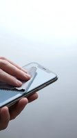 Hands cleaning smartphone screen with microfiber cloth against white background for hygiene and device maintenance.
