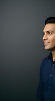 Young man with dark hair and olive complexion wearing navy blue shirt, smiling in profile against neutral gray background for corporate and business applications.