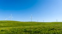 Wind turbines on rolling green hills under clear blue sky, renewable energy landscape for sustainable power generation projects.
