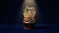 Chocolate cupcake with golden crown topper and Happy Birthday inscription, illuminated by spotlight on dark blue background, festive celebration concept.
