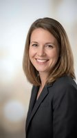Professional Caucasian businesswoman with brown hair smiling confidently in dark blazer for corporate headshot and business marketing materials.