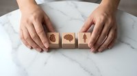Hands arranging wooden blocks with heart, brain, and body icons on marble surface, representing holistic health, wellness balance, and integrated medical care approach.