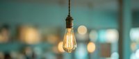 Vintage Edison bulb hanging from rope cord with warm filament glow against blurred modern interior background for creative lighting design concepts.