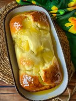 Homemade bread pudding with vanilla custard sauce in baking dish, golden brown brioche soaked in rich egg mixture, topped with warm caramel drizzle.