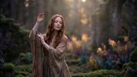 Young redhead woman in earth-tone robes practicing mystical gestures in enchanted forest setting with magical bokeh lighting for fantasy storytelling.