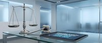 Modern legal office with brass scales of justice and digital tablet on glass desk in contemporary workspace for law firm branding.