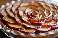 Caramelized apple tart with spiral pattern arrangement shows thinly sliced fruit layered in concentric circles, glazed to golden brown perfection in flaky pastry crust.