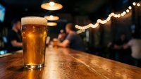Golden beer glass on wooden bar counter in cozy pub with warm lighting and bokeh background creating inviting atmosphere for social gatherings and nightlife.