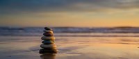Balanced stone stack on wet beach sand during golden hour sunset with calm ocean waves and colorful sky reflection creating peaceful meditation scene.