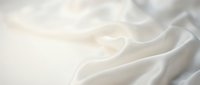 Soft white silk fabric with elegant flowing folds and gentle waves creating luxurious textile background for fashion and interior design projects.