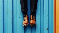 Levitating brown leather oxford shoes against vibrant blue wooden wall background, black pants visible, creating surreal floating effect for creative fashion concept.