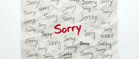 Crumpled paper covered with the word Sorry written repeatedly in various fonts, with one bold red Sorry in the center, expressing apology and regret.