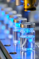 Medical vials with clear liquid on production line illuminated by blue light, showing pharmaceutical manufacturing process with selective focus.