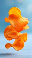 Flying crispy potato chips in motion against blue background, bright orange color with natural texture and shadows, appetizing snack food photography.