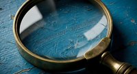 Vintage brass magnifying glass on weathered blue wooden surface with scratches and worn paint texture for detective mystery investigation concepts.