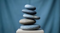 Balanced stack of smooth river stones creating zen meditation tower on wooden surface with soft blue background for wellness and mindfulness concepts.