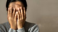 Young Asian woman covering face with hands expressing stress, anxiety, depression, shame or emotional overwhelm in mental health concept.