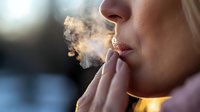Young woman exhaling smoke in golden sunset light, close up view of female lips and nose with dramatic atmospheric lighting and vapor clouds.