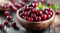Fresh ripe cranberries in wooden bowl on rustic table, garnished with green leaves. Bright red berries with natural lighting and selective focus.