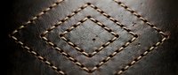 Brown leather surface with decorative diamond-shaped stitching pattern in contrasting thread creating geometric design for luxury craftsmanship backgrounds.