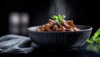 Steaming hot braised meat in dark ceramic bowl garnished with fresh herbs, served on black background with rising vapor and dramatic lighting for food photography.