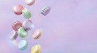 Colorful macarons falling through air on soft pink gradient background. French pastry dessert cookies in pastel colors creating dynamic motion composition.