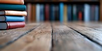 Stack of colorful hardcover books on rustic wooden table with blurred bookshelf background, shallow depth of field creates dreamy atmosphere for education concept.