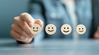 Business person selecting wooden smile face emoticon on blue background, representing customer satisfaction and positive feedback in service evaluation.